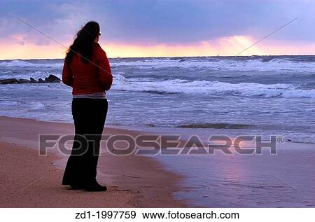A woman looks at dramatic storm clouds during winter sunset at sea. View Large Photo Image Stock Photo - A woman looks at dramatic storm clouds during winter sunset at sea.. Fotosearch