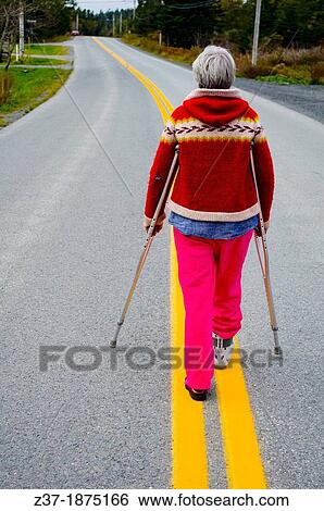 A woman on crutches with an injured foot surveys the long road ahead, Nova Scotia, Canada View Large Photo Image Stock Photograph - A woman on crutches with an injured foot surveys the long road ahead, Nova Scotia, Canada. Fotosearch