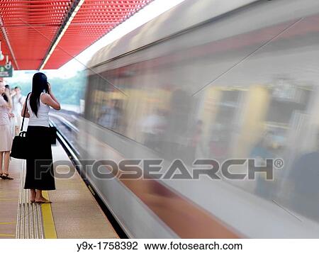 Stock Image - A woman on her phone as the MRT passes by in Singapore The Mass Rapid Transit MRT is one of the main modes of public transport in Singapore and handles up to a third of the nation's population everyday. Fotosearch