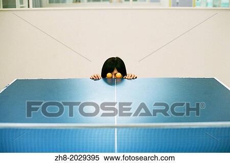 A woman poses with two orange ping pong balls as eyes at the edge of a ping pong table. View Large Photo Image Stock Photography - A woman poses with two orange ping pong balls as eyes at the edge of a ping pong table.. Fotosearch