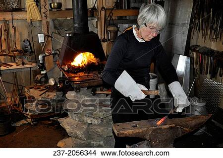 Picture - A woman prepares to strike a red hot iron bar in a small forge, Nova Scotia, Canada. Fotosearch