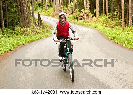 a woman rides a bicycle on a road through a forest View Large Photo Image Stock Image - a woman rides a bicycle on a road through a forest. Fotosearch