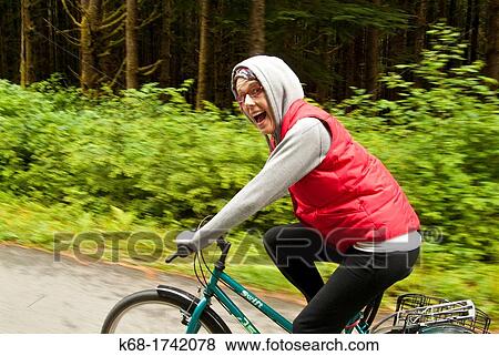 a woman rides a bicycle on a road through a forest View Large Photo Image Stock Photo - a woman rides a bicycle on a road through a forest. Fotosearch
