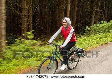 a woman rides a bicycle on a road through a forest View Large Photo Image Stock Photo - a woman rides a bicycle on a road through a forest. Fotosearch
