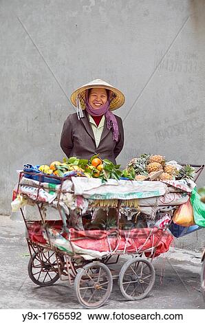Stock Image - A woman selling fruits from a cart in a back alley of Vietnam. Fotosearch