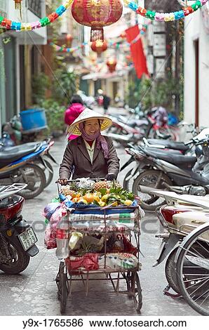 Stock Photograph - A woman selling fruits from a cart in a back alley of Vietnam. Fotosearch