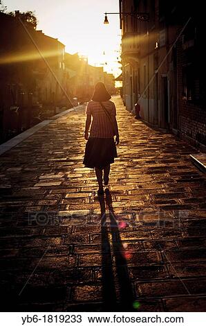 Stock Image - A woman wearing a hat walking in the Cannargeio during sunset time, Venice, Italy. Fotosearch