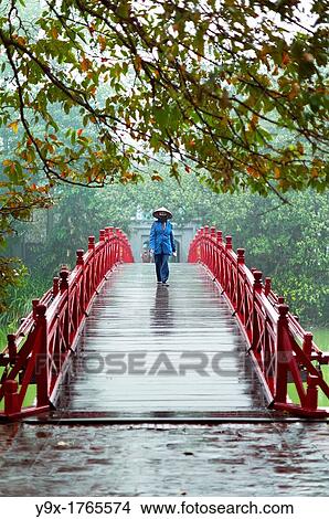 Picture - A woman wearing a traditional Non La hat on the red bridge at the Hoan Kiem Lake in Vietnam. Fotosearch