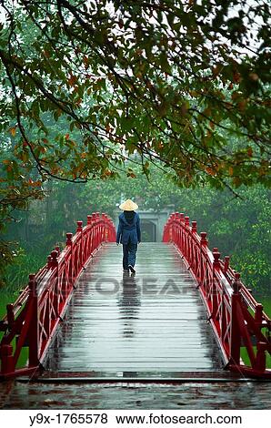 A woman wearing a traditional Non La hat on the red bridge at the Hoan Kiem Lake in Vietnam View Large Photo Image Stock Photo - A woman wearing a traditional Non La hat on the red bridge at the Hoan Kiem Lake in Vietnam. Fotosearch