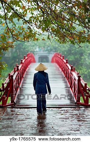 A woman wearing a traditional Non La hat on the red bridge at the Hoan Kiem Lake in Vietnam View Large Photo Image Stock Photography - A woman wearing a traditional Non La hat on the red bridge at the Hoan Kiem Lake in Vietnam. Fotosearch