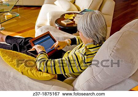 Stock Photo - A woman with a tablet relaxes in her well-appointed living room, Etobicoke, Canada. Fotosearch