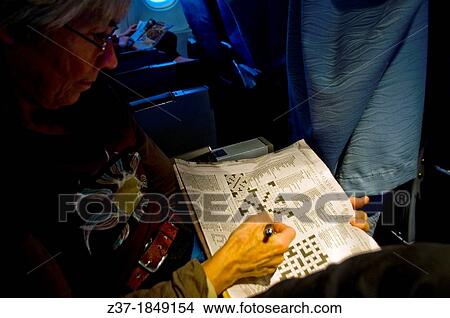 Picture - A woman works on a crossword on board a plane in flight. Fotosearch