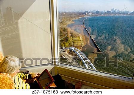 Stock Photo - A woman works with her IPAD overlooking the Toronto skyline, Ontario, Canada. Fotosearch