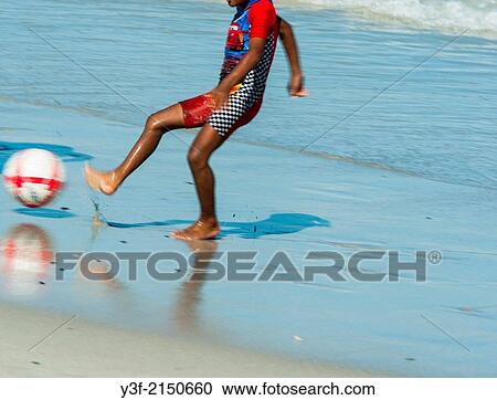 A young African lad dressed in a sun-protective bathing suit, kicks a ball on the beach at low tide. Cape Town South Africa View Large Photo Image Stock Image - A young African lad dressed in a sun-protective bathing suit, kicks a ball on the beach at low tide. Cape Town South Africa. Fotosearch