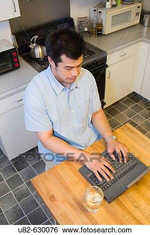 A young Asian-American man using a laptop computer wirelessly at home. View Large Photo Image Stock Photograph - A young Asian-American man using a laptop computer wirelessly at home.. Fotosearch