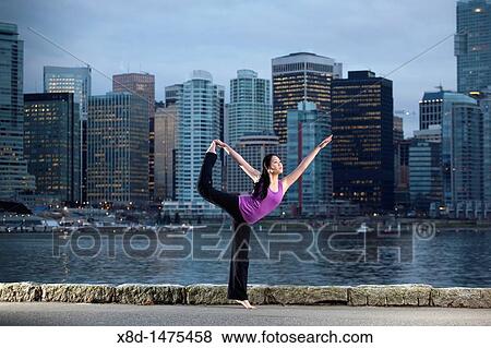 A young Asian woman does the Natarajasana Lord of the Dance yoga pose along the Stanley Park seawall with the city skyline beyond, Vancouver, British Columbia, Canada View Large Photo Image Stock Photo - A young Asian woman does the Natarajasana Lord of the Dance yoga pose along the Stanley Park seawall with the city skyline beyond, Vancouver, British Columbia, Canada. Fotosearch