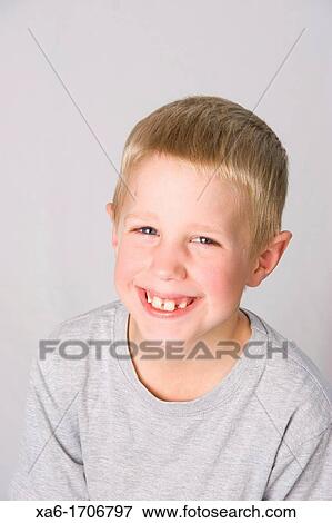 Stock Photo - A young blond boy smiles widely at the camera against a grey background. Fotosearch