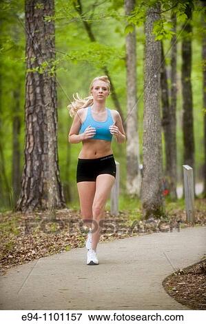Stock Photo - A young blond woman jogging toward camera on an asphalt path in a park.. Fotosearch