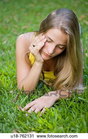 Stock Image - a young blonde girl laying down in the grass with a yellow shirt. Fotosearch