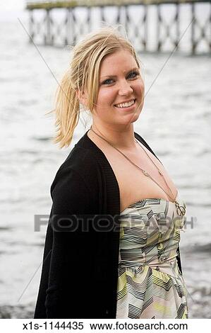 A young blonde on a beach looking toward the camera with water and wooden pier in the background View Large Photo Image Stock Photography - A young blonde on a beach looking toward the camera with water and wooden pier in the background. Fotosearch