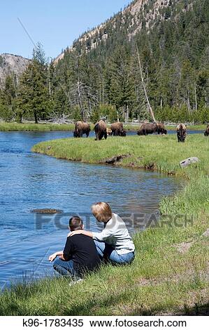 Stock Photography - a young boy and a woman sitting along a river overlooking buffalo. Fotosearch