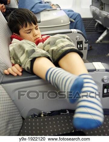 A young boy asleep on an airplane with his legs propped on the armrests View Large Photo Image Stock Image - A young boy asleep on an airplane with his legs propped on the armrests. Fotosearch