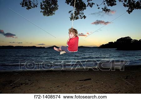A young boy on a rope swing at dusk under a Pohutukawa tree at Oamaru Bay, Coromandel Peninsula, North Island, New Zealand View Large Photo Image Picture - A young boy on a rope swing at dusk under a Pohutukawa tree at Oamaru Bay, Coromandel Peninsula, North Island, New Zealand. Fotosearch
