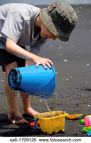 Stock Photograph - A young boy plays on the beach with water and buckets. Fotosearch