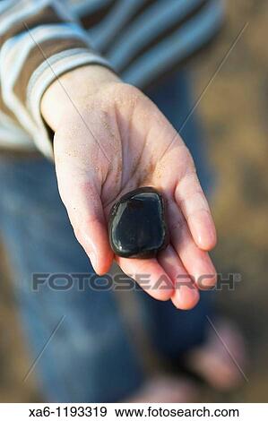 A young boy's sandy hand holds a shiny wet black stone View Large Photo Image Stock Photo - A young boy's sandy hand holds a shiny wet black stone. Fotosearch