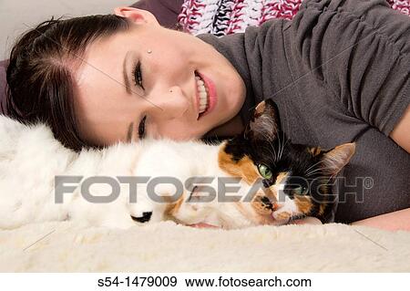 Stock Photo - A young caucasian woman and her calico cat indoors. Fotosearch