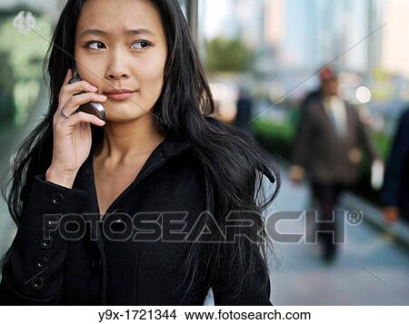A young Chinese business woman using her mobile phone in the city View Large Photo Image Picture - A young Chinese business woman using her mobile phone in the city. Fotosearch