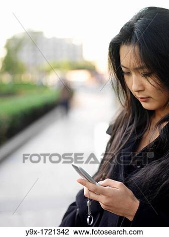 Stock Image - A young Chinese business woman using her mobile phone in the city. Fotosearch