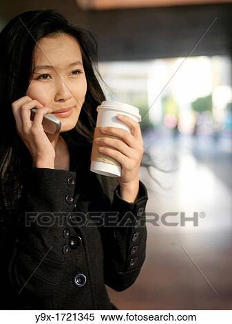 A young Chinese business woman using her mobile phone in the city as she sips on a beverage in a disposable cup View Large Photo Image Stock Photography - A young Chinese business woman using her mobile phone in the city as she sips on a beverage in a disposable cup. Fotosearch