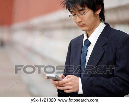 A young Chinese businessman in a shirt with a suit over his shoulder checking his text messages or email on his mobile smart phone through wireless internet with traditional Chinese architecure in the background in Beijing View Large Photo Image Stock Image - A young Chinese businessman in a shirt with a suit over his shoulder checking his text messages or email on his mobile smart phone through wireless internet with traditional Chinese architecure in the background in Beijing. Fotosearch