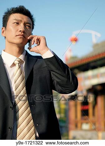 A young Chinese businessman in a suit talking on his phone on business projects with Chinese traditional architecture in the background in Beijing View Large Photo Image Stock Image - A young Chinese businessman in a suit talking on his phone on business projects with Chinese traditional architecture in the background in Beijing. Fotosearch