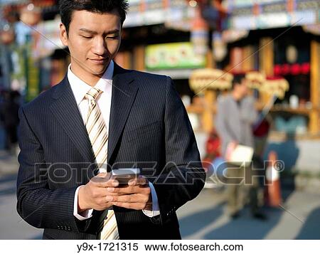 A young Chinese businessman in a suit checking his text messages or email on his mobile smart phone through wireless internet with traditional Chinese architecure in the background in Beijing View Large Photo Image Stock Photography - A young Chinese businessman in a suit checking his text messages or email on his mobile smart phone through wireless internet with traditional Chinese architecure in the background in Beijing. Fotosearch