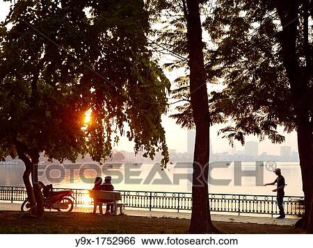A young couple embraces on a park bench overlooking Hanoi's West Lake, one of the few natural escapes within the bustling city View Large Photo Image Stock Photograph - A young couple embraces on a park bench overlooking Hanoi's West Lake, one of the few natural escapes within the bustling city. Fotosearch