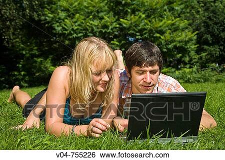 A young couple is lying in the grass looking at their laptop computer outdoors View Large Photo Image Stock Photograph - A young couple is lying in the grass looking at their laptop computer outdoors. Fotosearch