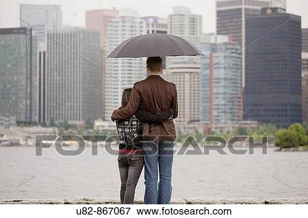 A young couple looking at the city skyline under an umbrella on a rainy day, Vancouver, British Columbia, Canada View Large Photo Image Stock Photo - A young couple looking at the city skyline under an umbrella on a rainy day, Vancouver, British Columbia, Canada. Fotosearch