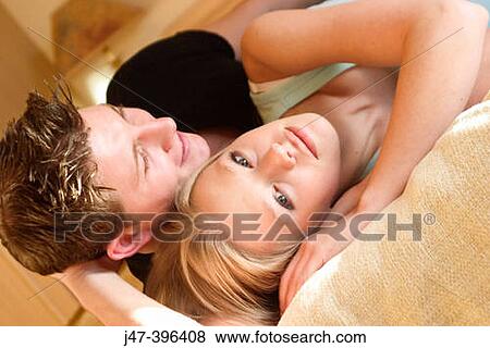 Stock Photo - A young couple lying on a bed, her looking straight into camera. Fotosearch