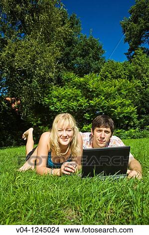 A young couple lying outside on the grass with their laptop computer View Large Photo Image Picture - A young couple lying outside on the grass with their laptop computer. Fotosearch