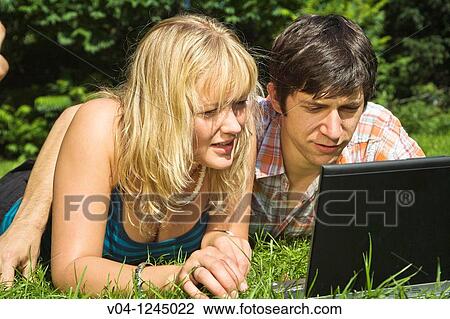 A young couple lying outside on the grass looking at their laptop computer View Large Photo Image Stock Image - A young couple lying outside on the grass looking at their laptop computer. Fotosearch