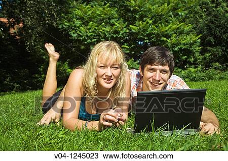 A young couple lying outside on the grass with their laptop computer View Large Photo Image Stock Image - A young couple lying outside on the grass with their laptop computer. Fotosearch