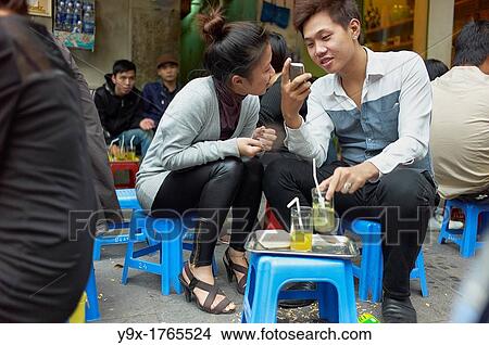 A young couple seated at an outdoor cafe laughing and smiling while looking at their cell phone View Large Photo Image Picture - A young couple seated at an outdoor cafe laughing and smiling while looking at their cell phone. Fotosearch