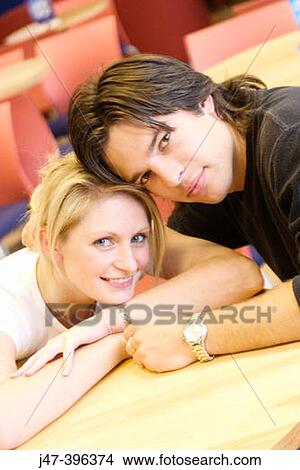 A young couple sitting in a cafe heads together, smiling into camera View Large Photo Image Picture - A young couple sitting in a cafe heads together, smiling into camera. Fotosearch
