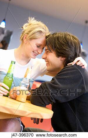 A young couple sitting in a cafe heads together, smiling at each other View Large Photo Image Stock Image - A young couple sitting in a cafe heads together, smiling at each other. Fotosearch