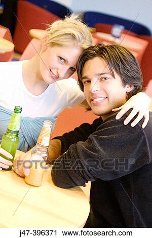 A young couple sitting in a cafe heads together, smiling into camera View Large Photo Image Stock Image - A young couple sitting in a cafe heads together, smiling into camera. Fotosearch