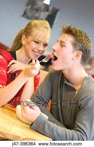 A young couple sitting in a cafe sharing a bowl of fruit smiling, shes feeding him View Large Photo Image Picture - A young couple sitting in a cafe sharing a bowl of fruit smiling, shes feeding him. Fotosearch