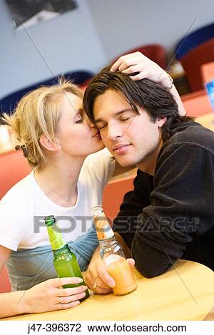A young couple sitting in a cafe she's kissing his ear, he's smiling with his eyes closed View Large Photo Image Stock Image - A young couple sitting in a cafe she's kissing his ear, he's smiling with his eyes closed. Fotosearch