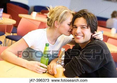 A young couple sitting in a cafe she's whispering in his ear, he's smiling into camera View Large Photo Image Stock Image - A young couple sitting in a cafe she's whispering in his ear, he's smiling into camera. Fotosearch